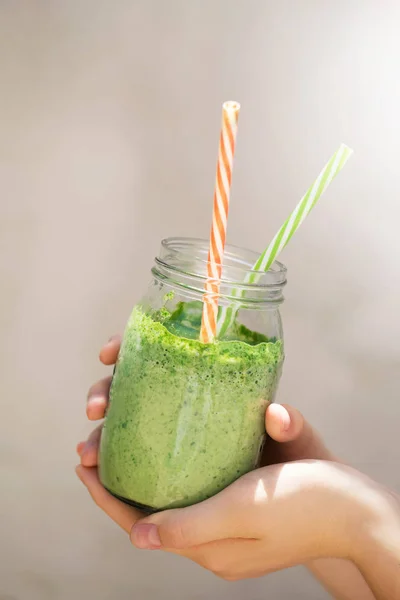 Summer healthy detox drink, blended green smoothie in the bright midday, in the hands of a girl, selective focus