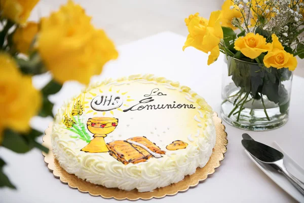 first holy communion concept, beautiful cake with text in italian: first holy communion and yellow roses on a white table