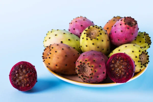 Bir tabakta bütün taze dikenli armut meyve ve bir pastel mavi arka plan üzerinde yarım opuntia kesti. Minimalizm