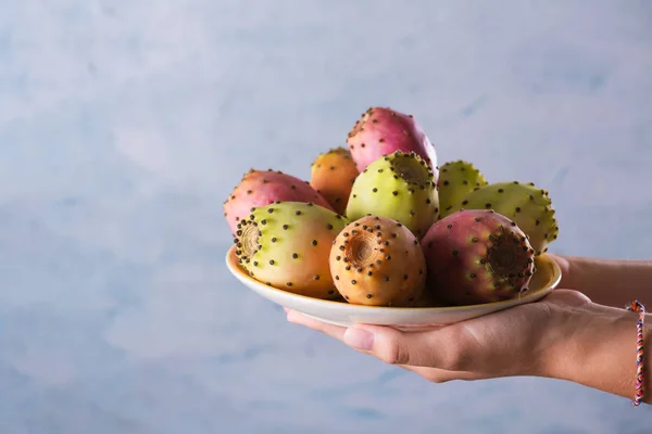 Frauenhände halten einen Teller mit reifen frischen Früchten der Kaktusfeige auf grauem Hintergrund, selektiver Fokus — Stockfoto