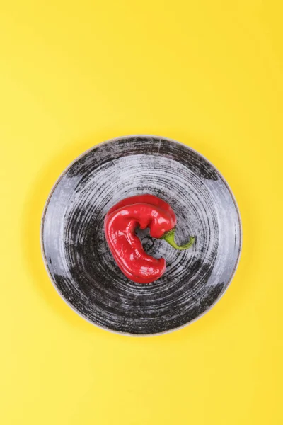 Brutti peperoncini rossi su un piatto nero su sfondo giallo, stile minimale della natura, pop art, concetto di cibo creativo, arte moderna — Foto Stock