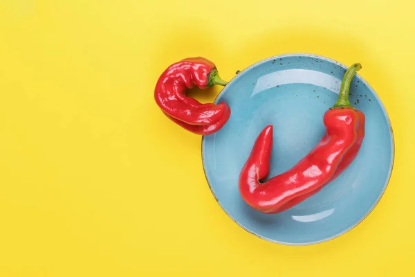 Brutti peperoncini rossi su un piatto turchese su sfondo giallo, stile minimale della natura, pop art, concetto di cibo creativo, arte moderna — Foto Stock