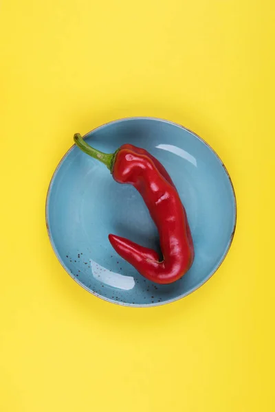 Brutti peperoncini rossi su un piatto blu su sfondo giallo, stile minimale della natura, pop art, concetto di cibo creativo, arte moderna — Foto Stock