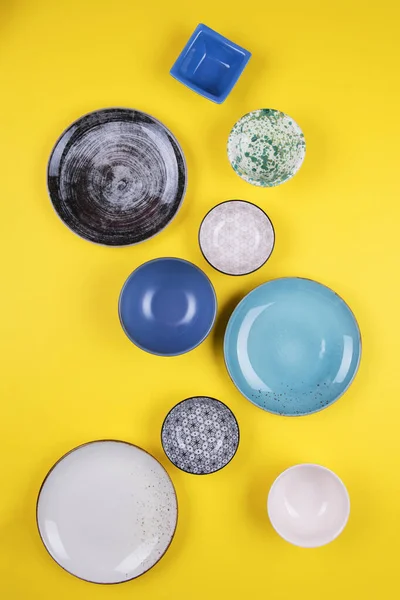 Набор красочных современных фарфоровых тарелок и чаш на желтом фоне. дизайнер керамики различных цветов: синий, бирюзовый, серый и темно-синий — стоковое фото