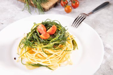 İtalyan baharında sebzeli spagetti ve gri arka planda beyaz bir tabakta çatal ve malzemeler.