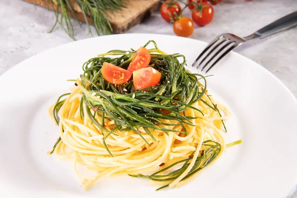 İtalyan baharında sebzeli spagetti ve gri arka planda beyaz bir tabakta çatal ve malzemeler.