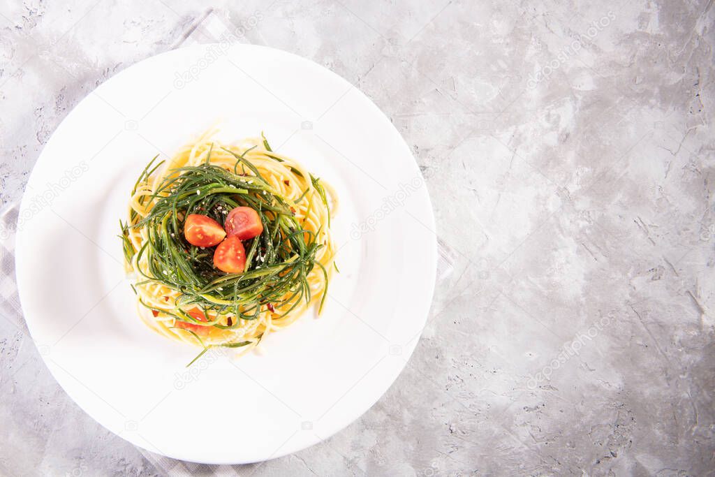 Spaghetti with agretti, a spring vegetable from Italy, on a white plate on a gray background, above