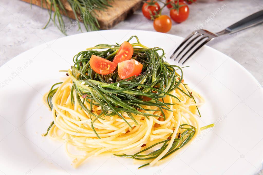 Spaghetti with agretti, a spring vegetable from Italy, and and ingredients and fork on a white plate on a gray background