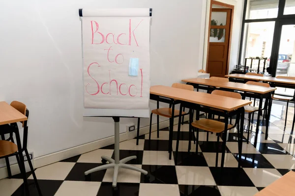 A whiteboard in empty classroom with lettering Back to school and medical mask attach, school life during Covid-19 pandemic, new normal. Returning to school after quarantine, happiness and hope