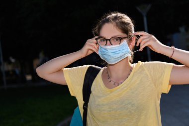 Gözlüklü genç bir kadın koruyucu bir maske takıyor. Coronavirus cihazlarını kapatıyor ve sosyal mesafeli, seçici bir odaklanma sürecinde yeni normal bir hayat sürüyor.