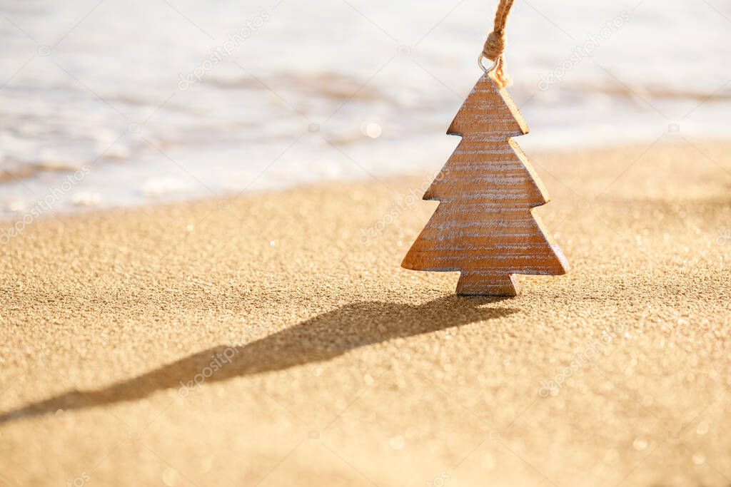 Timber wooden decoration of Christmas tree on a sand on the tropical beach near ocean, summer Christmas and winter holyday concept, selective focus. Happy New Year background. Zero waste Christmas