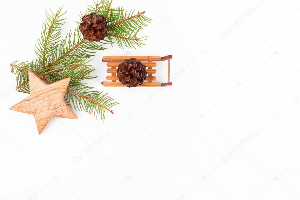 Christmas background frame of fir twigs, wooden zero waste home decotarion: sleigh, stars and chistmas tree on white background, top view. Reusable sustainable recycled decor. Eco friendly new year