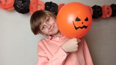 Sarışın bir çocuk balon sallayarak eğleniyor. Jack 'O Lantern' ın yüzüyle evde oynuyor. Cadılar Bayramı süsleriyle evde oynuyor.