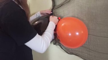 Kız duvara iki tane siyah ve turuncu balon yapıştırıyor, Cadılar Bayramı için evi dekore ediyor, Cadılar Bayramı için evde hazırlanıyor,