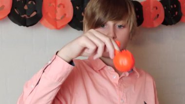 Sarışın bir çocuk balonunu sallayarak eğleniyor Jack O 'Lantern' ın yüzüyle, balonu şişiriyor, Cadılar Bayramı süsleriyle evde