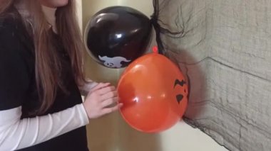 Kız duvara iki tane siyah ve turuncu balon yapıştırıyor, bir balon düşüyor, Cadılar Bayramı için evi dekore ediyor, cadılar bayramı için evde hazırlanıyor,