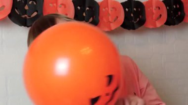 Sarışın bir çocuk balon sallayarak eğleniyor. Jack 'O Lantern' ın yüzüyle evde oynuyor. Cadılar Bayramı süsleriyle evde oynuyor.