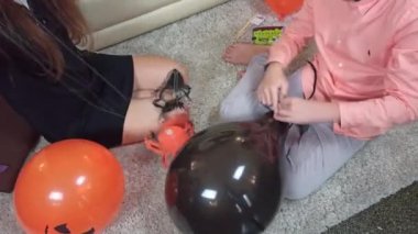 Evi süslemek için elinde örümceklerle kağıt bir çelenk tutan bir kız, balon bağlayan bir oğlan. Çocuklar Cadılar Bayramı 'nı evde kutlamaya hazır olun.