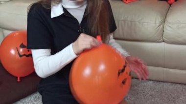Kız turuncu bir hallowen balonunu şişirip bağlıyor. Çocuklar Cadılar Bayramı 'nı evde kutlamak için evlerini dekore ederler.