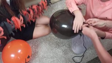 Evi süslemek için elinde örümceklerle kağıt bir çelenk tutan bir kız, balon bağlayan bir oğlan. Çocuklar Cadılar Bayramı 'nı evde kutlamaya hazır olun.