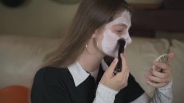 Bir kız Cadılar Bayramı için yüzünü beyaz makyajla boyuyor. Karnaval için ev makyajı, evde cadılar bayramı kutlaması.