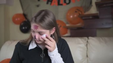 Bir kız yüzüne geçici bir dövme yaptırır, cadılar bayramı için basit bir makyaj. Cadılar Bayramı 'nı evde kutluyoruz.