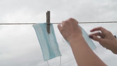 Tek kullanımlık tıbbi bir maskeyi kurutmak için takılan bir kadın, Gri sonbahar gökyüzünün arka planına karşı Covid-19 sırasında yeniden kullanılmak üzere yeni yıkandı.