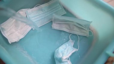 Tıbbi koruyucu maskelerin yıkanması. Su mavi bir lavaboya dökülüyor, çamaşır tozu dökülüyor. Coronavirus Covid-19 salgını sırasında yeni normaller