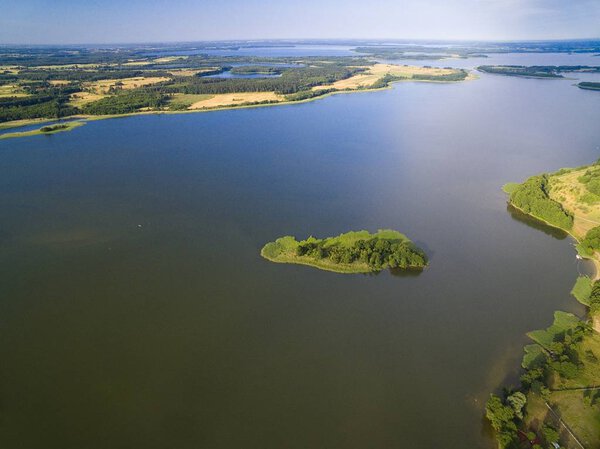Aerial view of small uninhabited island on lake with sky reflected in calm water, Swiecajty Lake, Mazury, Poland