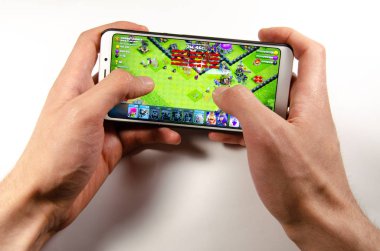 April, 2019. Kramatorsk, Ukraine. Clash of Clans gameplay on a white smartphone in hand clipart