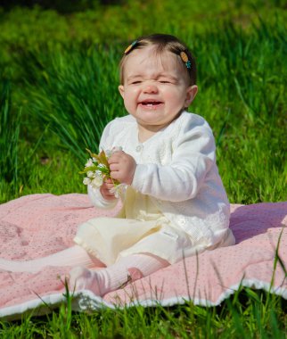 Parkta yeşil çim üzerinde pembe ekose parlak giysiler bebek. Yeni doğan bebek sıcak bir günde dışarıda. Küçük kız ilkbaharda yeşil bir çim enlaid üzerinde bir ekose üzerinde oynuyor