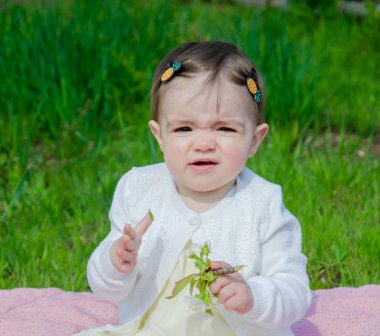 Parkta yeşil çim üzerinde pembe ekose parlak giysiler bebek. Yeni doğan bebek sıcak bir günde dışarıda. Küçük kız ilkbaharda yeşil bir çim enlaid üzerinde bir ekose üzerinde oynuyor