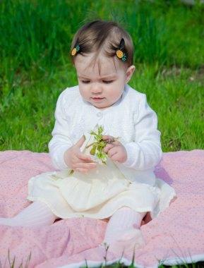 Parkta yeşil çim üzerinde pembe ekose parlak giysiler bebek. Yeni doğan bebek sıcak bir günde dışarıda. Küçük kız ilkbaharda yeşil bir çim enlaid üzerinde bir ekose üzerinde oynuyor