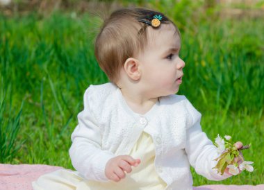Parkta yeşil çim üzerinde pembe ekose parlak giysiler bebek. Yeni doğan bebek sıcak bir günde dışarıda. Küçük kız ilkbaharda yeşil bir çim enlaid üzerinde bir ekose üzerinde oynuyor