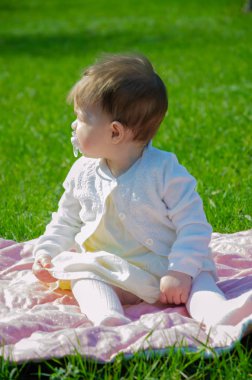 Parkta yeşil çim üzerinde pembe ekose parlak giysiler bebek. Yeni doğan bebek sıcak bir günde dışarıda. Küçük kız ilkbaharda yeşil bir çim enlaid üzerinde bir ekose üzerinde oynuyor