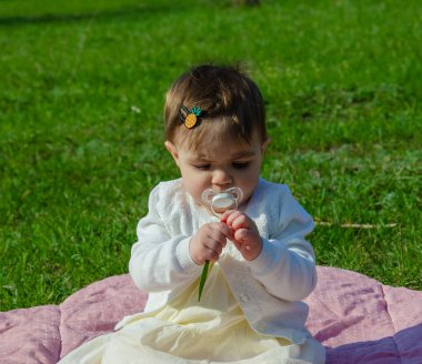 Parkta yeşil çim üzerinde pembe ekose parlak giysiler bebek. Yeni doğan bebek sıcak bir günde dışarıda. Küçük kız ilkbaharda yeşil bir çim enlaid üzerinde bir ekose üzerinde oynuyor