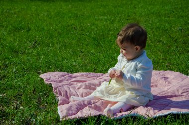 Parkta yeşil çim üzerinde pembe ekose parlak giysiler bebek. Yeni doğan bebek sıcak bir günde dışarıda. Küçük kız ilkbaharda yeşil bir çim enlaid üzerinde bir ekose üzerinde oynuyor