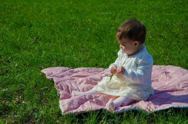Parkta yeşil çim üzerinde pembe ekose parlak giysiler bebek. Yeni doğan bebek sıcak bir günde dışarıda. Küçük kız ilkbaharda yeşil bir çim enlaid üzerinde bir ekose üzerinde oynuyor