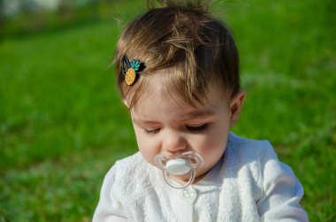 Parkta yeşil çim üzerinde pembe ekose parlak giysiler bebek. Yeni doğan bebek sıcak bir günde dışarıda. Küçük kız ilkbaharda yeşil bir çim enlaid üzerinde bir ekose üzerinde oynuyor