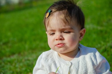 Parkta yeşil çim üzerinde pembe ekose parlak giysiler bebek. Yeni doğan bebek sıcak bir günde dışarıda. Küçük kız ilkbaharda yeşil bir çim enlaid üzerinde bir ekose üzerinde oynuyor