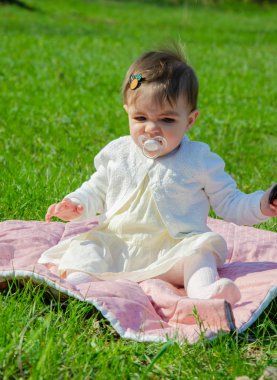 Parkta yeşil çim üzerinde pembe ekose parlak giysiler bebek. Yeni doğan bebek sıcak bir günde dışarıda. Küçük kız ilkbaharda yeşil bir çim enlaid üzerinde bir ekose üzerinde oynuyor
