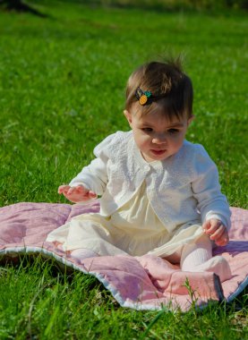 Parkta yeşil çim üzerinde pembe ekose parlak giysiler bebek. Yeni doğan bebek sıcak bir günde dışarıda. Küçük kız ilkbaharda yeşil bir çim enlaid üzerinde bir ekose üzerinde oynuyor