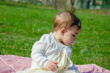 Parkta yeşil çim üzerinde pembe ekose parlak giysiler bebek. Yeni doğan bebek sıcak bir günde dışarıda. Küçük kız ilkbaharda yeşil bir çim enlaid üzerinde bir ekose üzerinde oynuyor