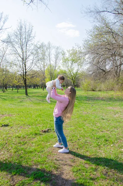 Mom with baby in bright clothes on a pink plaid on the green right. Family resting in the park on a warm day. Mom and little girl 10 months walk in the park