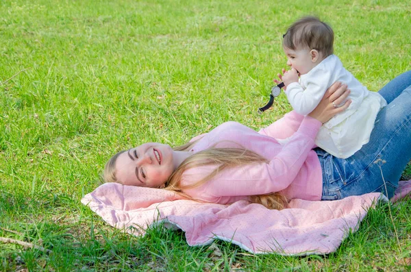 妈妈带着宝宝穿着鲜艳的衣服在绿色右边的粉红色格子上 一家人在温暖的一天在公园里休息 妈妈和小女孩10个月在公园散步 — 图库照片