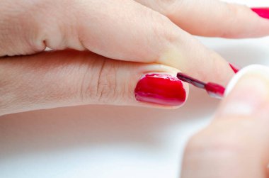 Evde manikür. Manikür. Kız tırnaklarını kırmızıya boyuyor, bordo. Parlak tırnak cilası. Makro 'da makro. Fırça, beyaz arka planda güçlü bir zum yaparak tırnağa vernik sürmektir.