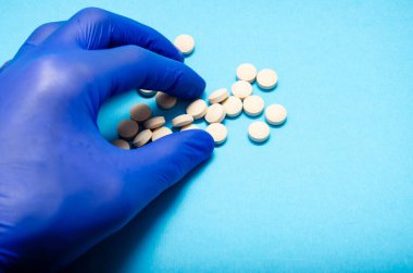 Mavi tıp eldivenlerini teslim eden bir adam mavi arka planda, parmaklarıyla bir tablet alıyor. El ve haplar 