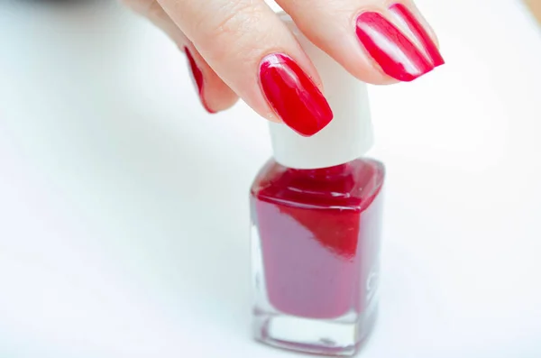 Manicure at home. DIY manicure. The girl paints herself nails in red, burgundy. Glossy nail polish. Hand holds bottle with nail polish.