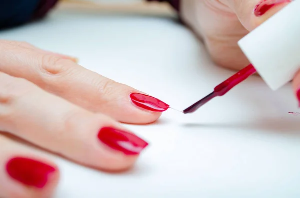 Manicure at home. DIY manicure. The girl paints herself nails in red, burgundy. Glossy nail polish. Macro in macro. Brush is applying varnish on the nail in a strong large zoom on a white background