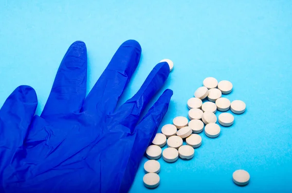A medical blue glove and white round pills lie on a blue background in macro view from above and at an angle. Crumpled glove